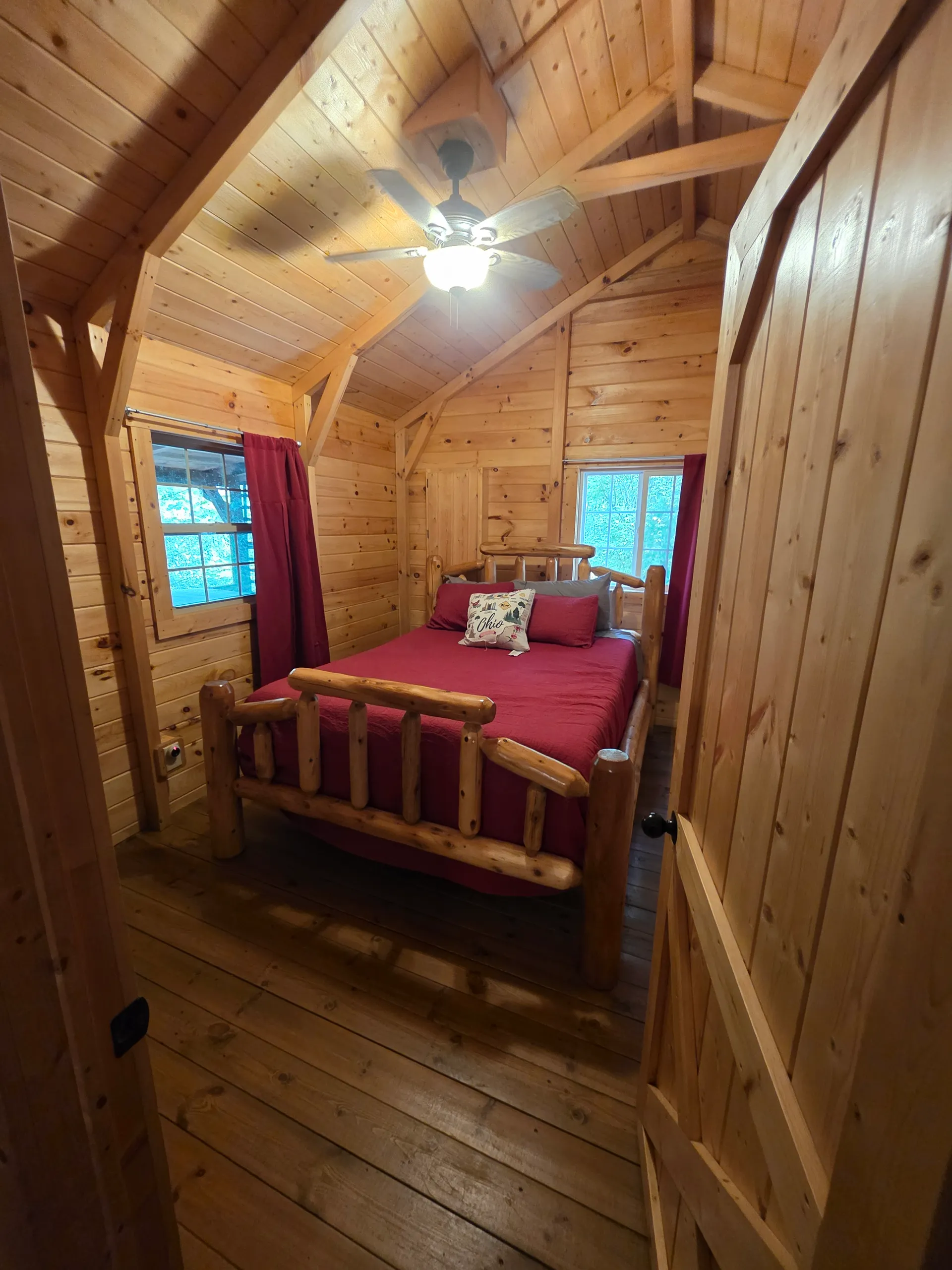 Loft bedroom with red bedspread and rustic log bed frame in the pine-paneled A-frame at Buckeye Hut cabin