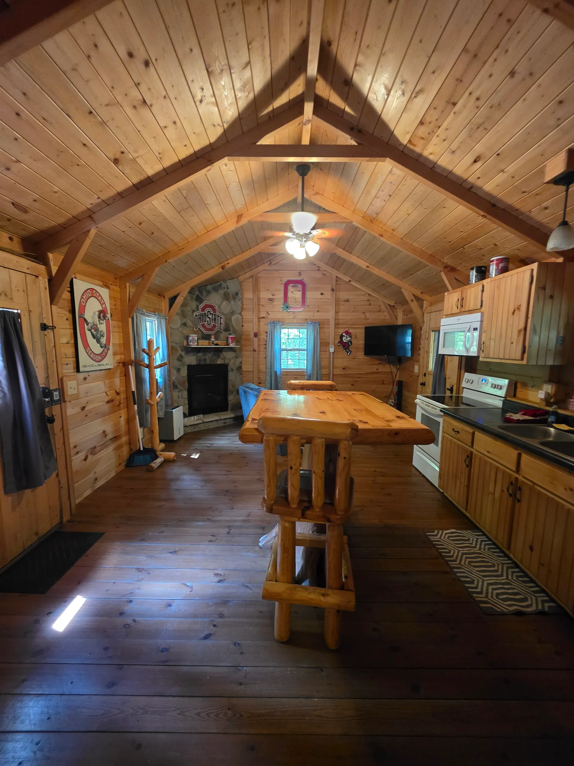Cozy pine-paneled living room with stone fireplace, log furniture, and vaulted ceiling at Buckeye Hut cabin