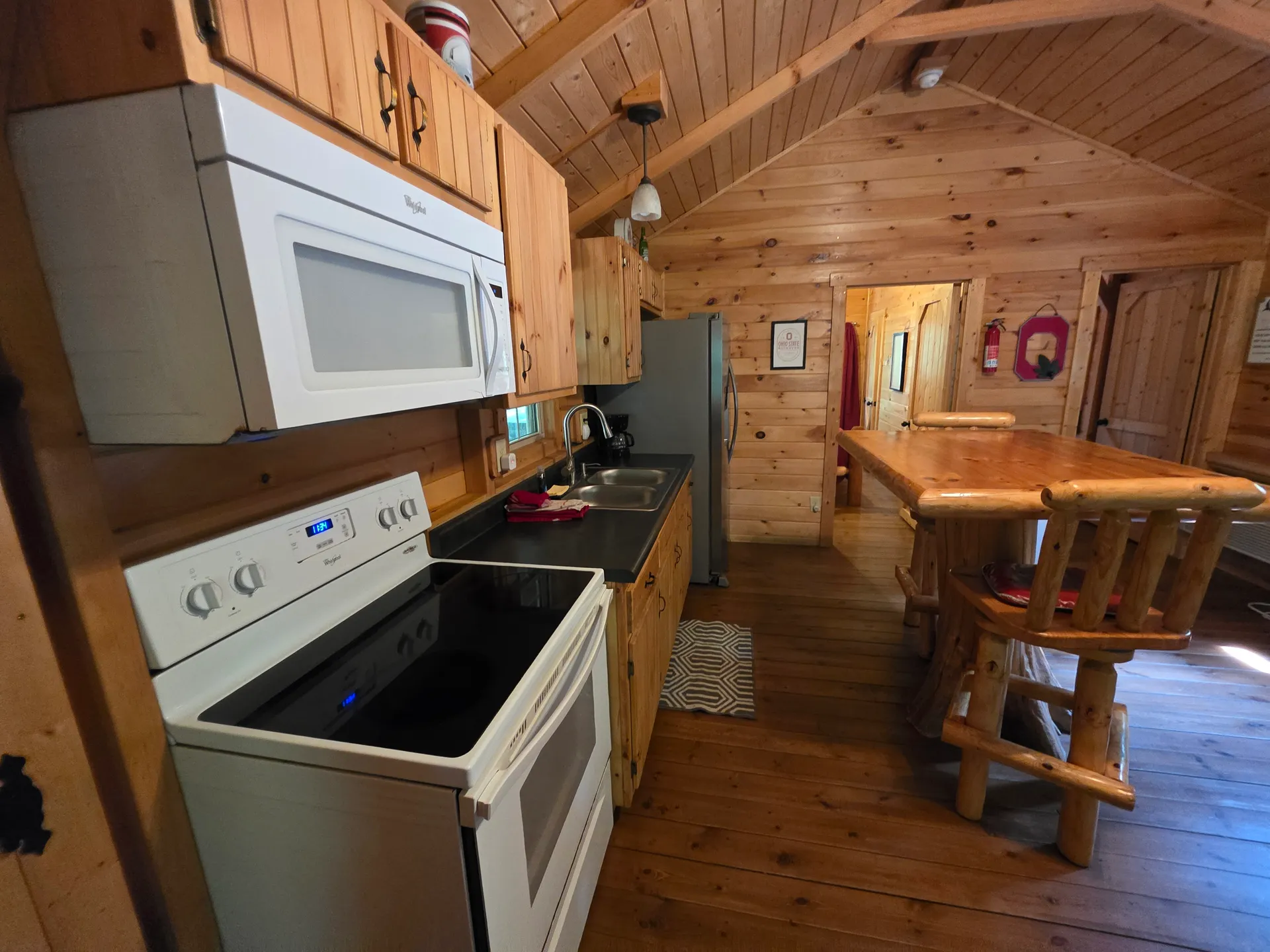 Full kitchen with pine cabinets, stove, microwave, and log bar stools at Buckeye Hut cabin