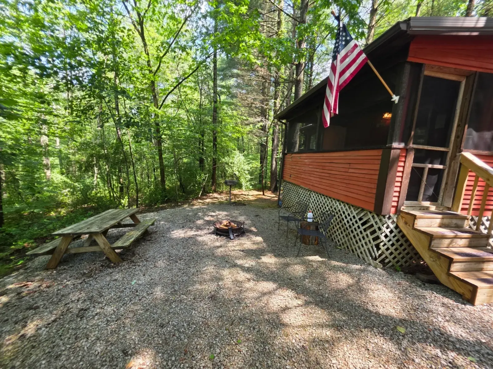 Side view of Cherokee Way cabin with fire pit, picnic table, and American flag among the trees