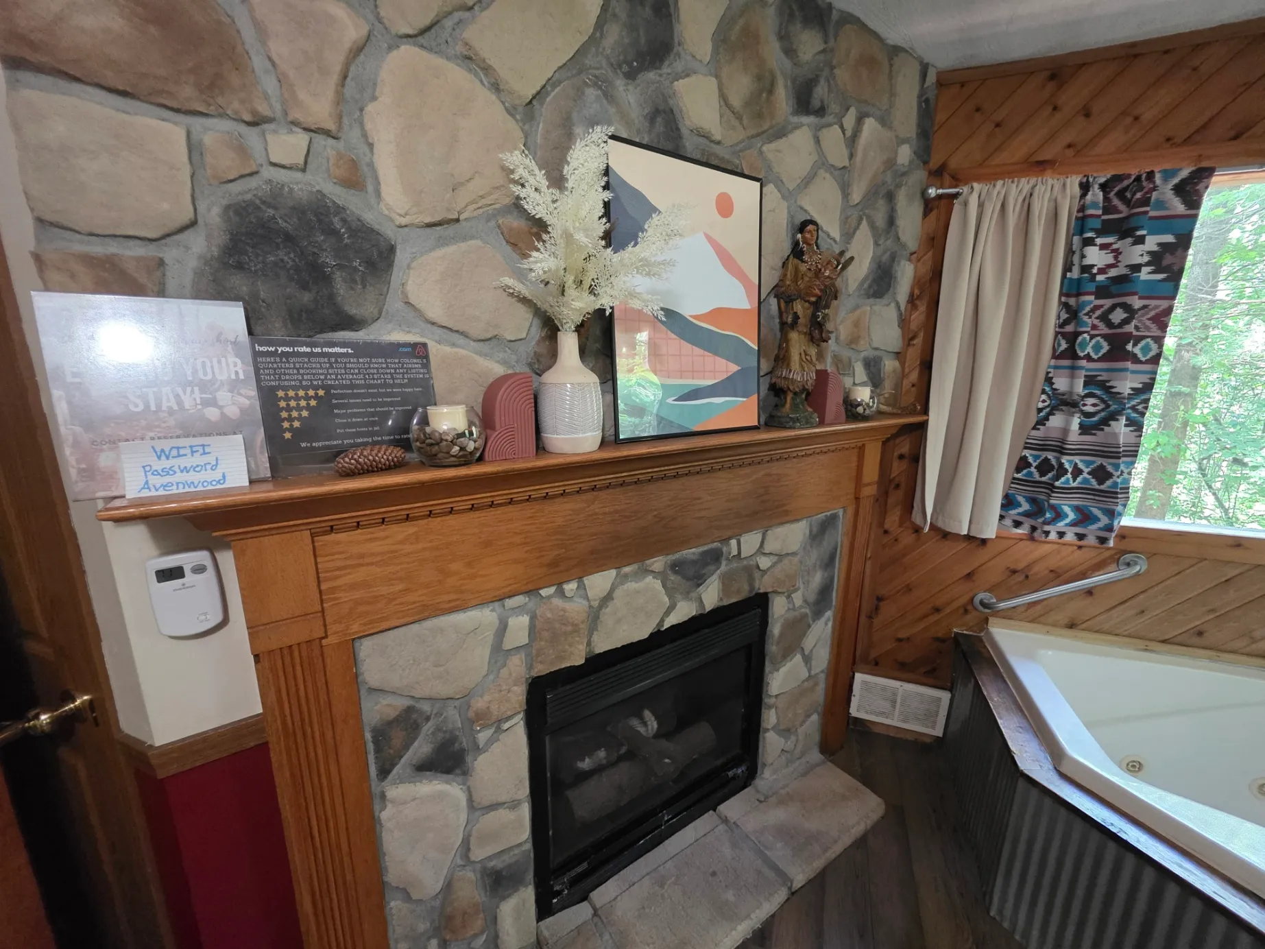 Stone fireplace with art print and figurine on wooden mantel next to jacuzzi at Cherokee Way cabin