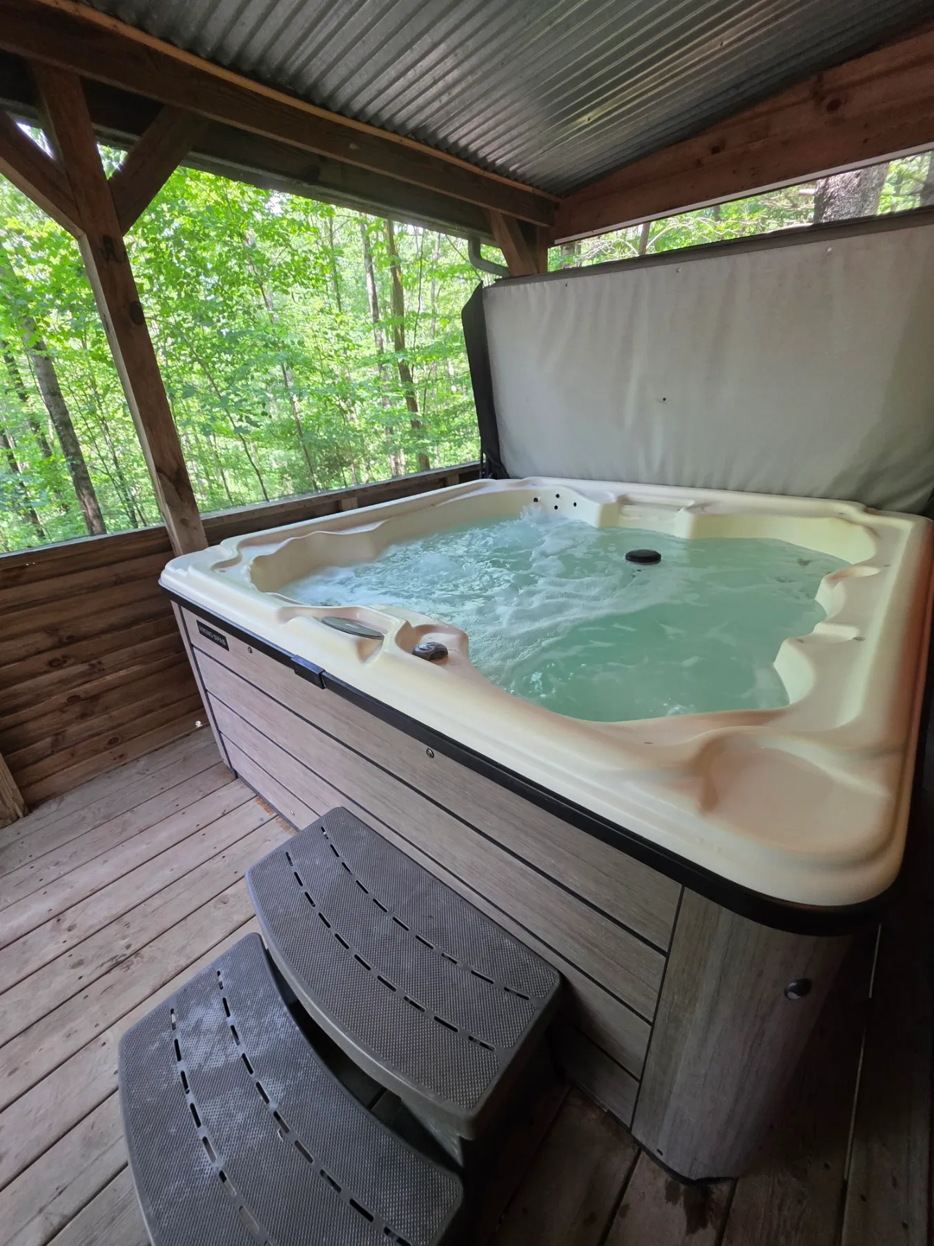 Hot tub on covered deck with forest views through lattice screening at Cherokee Way cabin