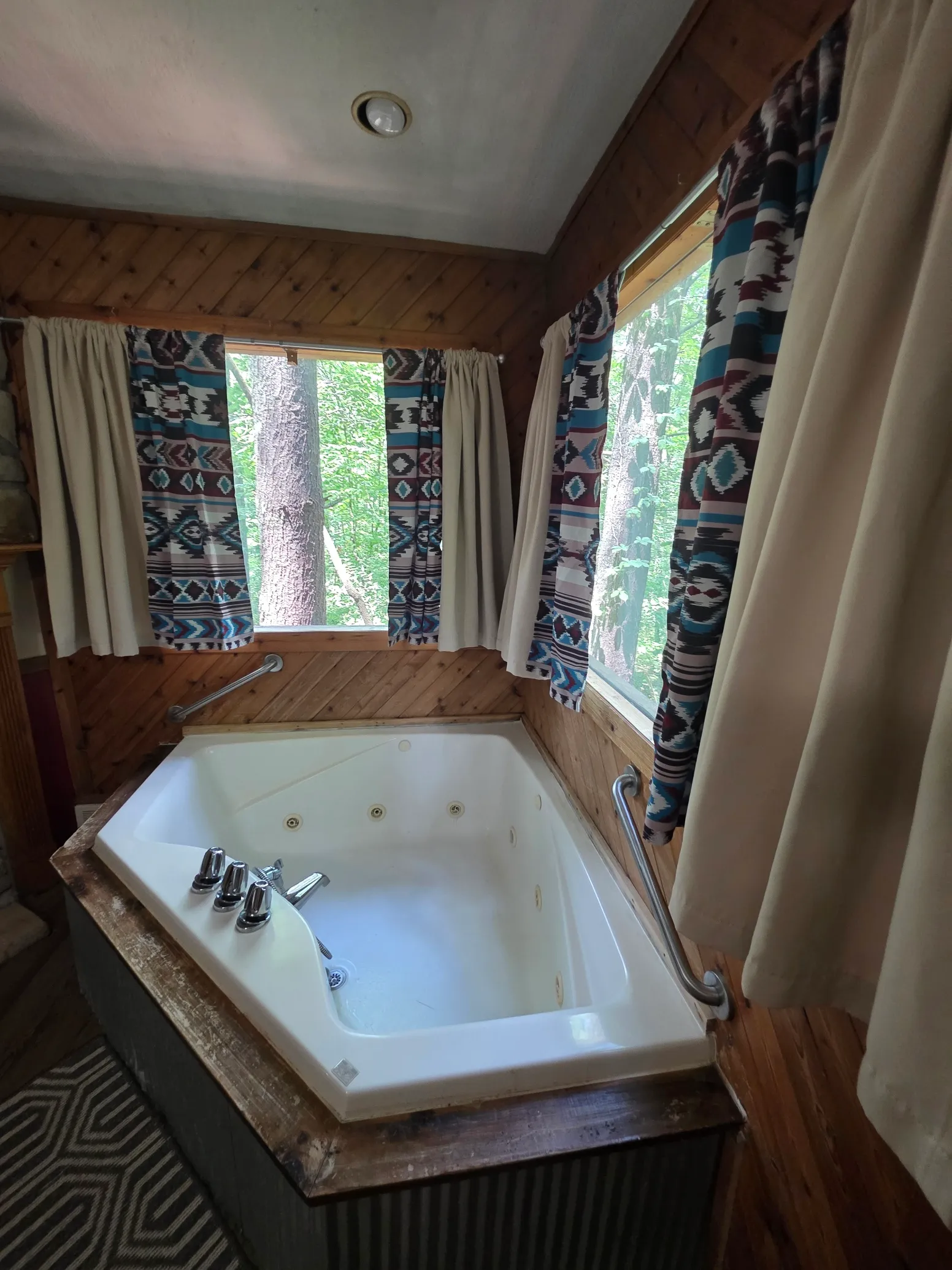 Overhead view of corner jacuzzi tub with patterned curtains and forest views at Cherokee Way cabin