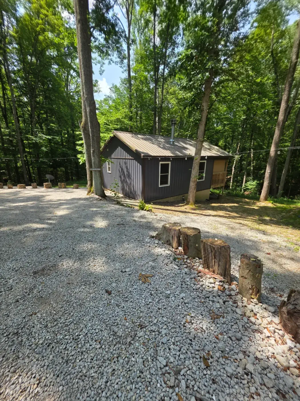Front of Dogwood Run cabin with gravel pad and log stumps in summer