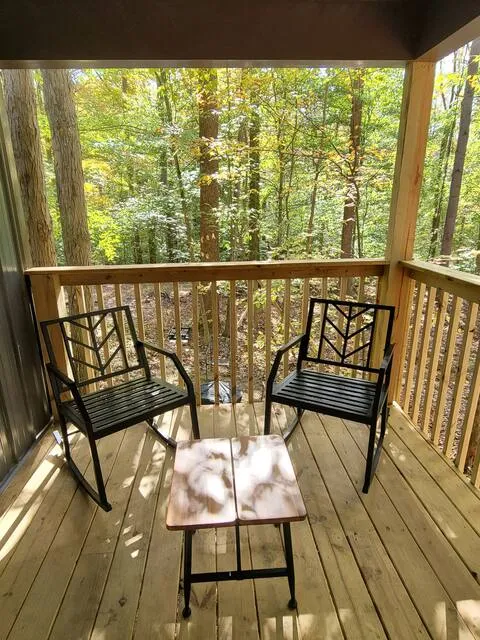 Covered porch with two metal chairs and small table overlooking the forest at Dogwood Run cabin