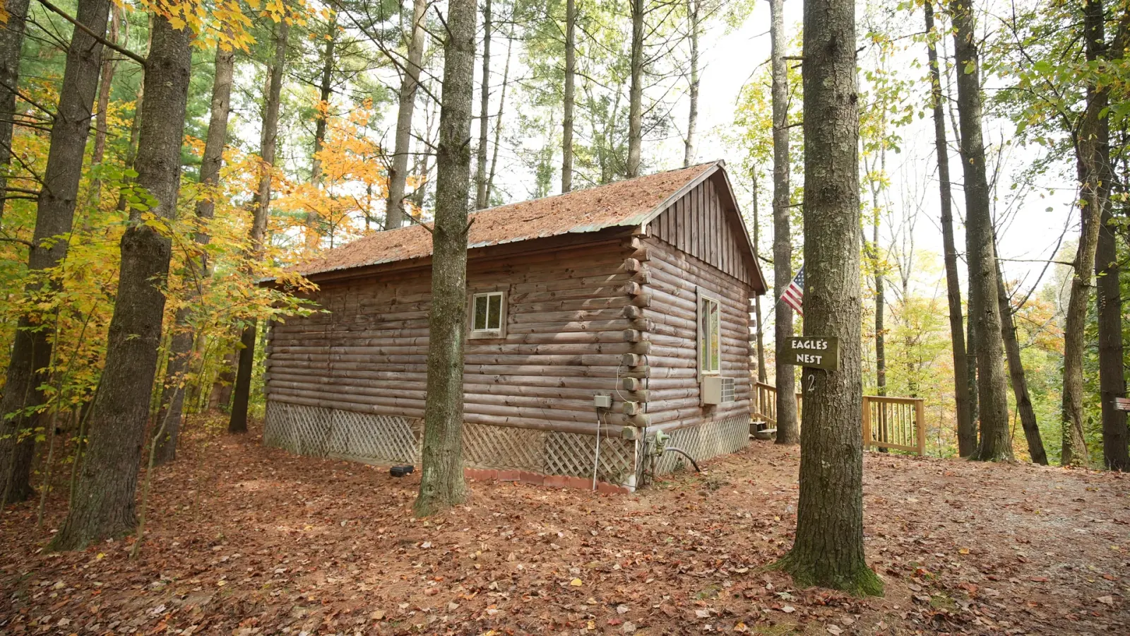 Front view of Eagles Nest log cabin with deck and American flag among autumn trees in Hocking Hills