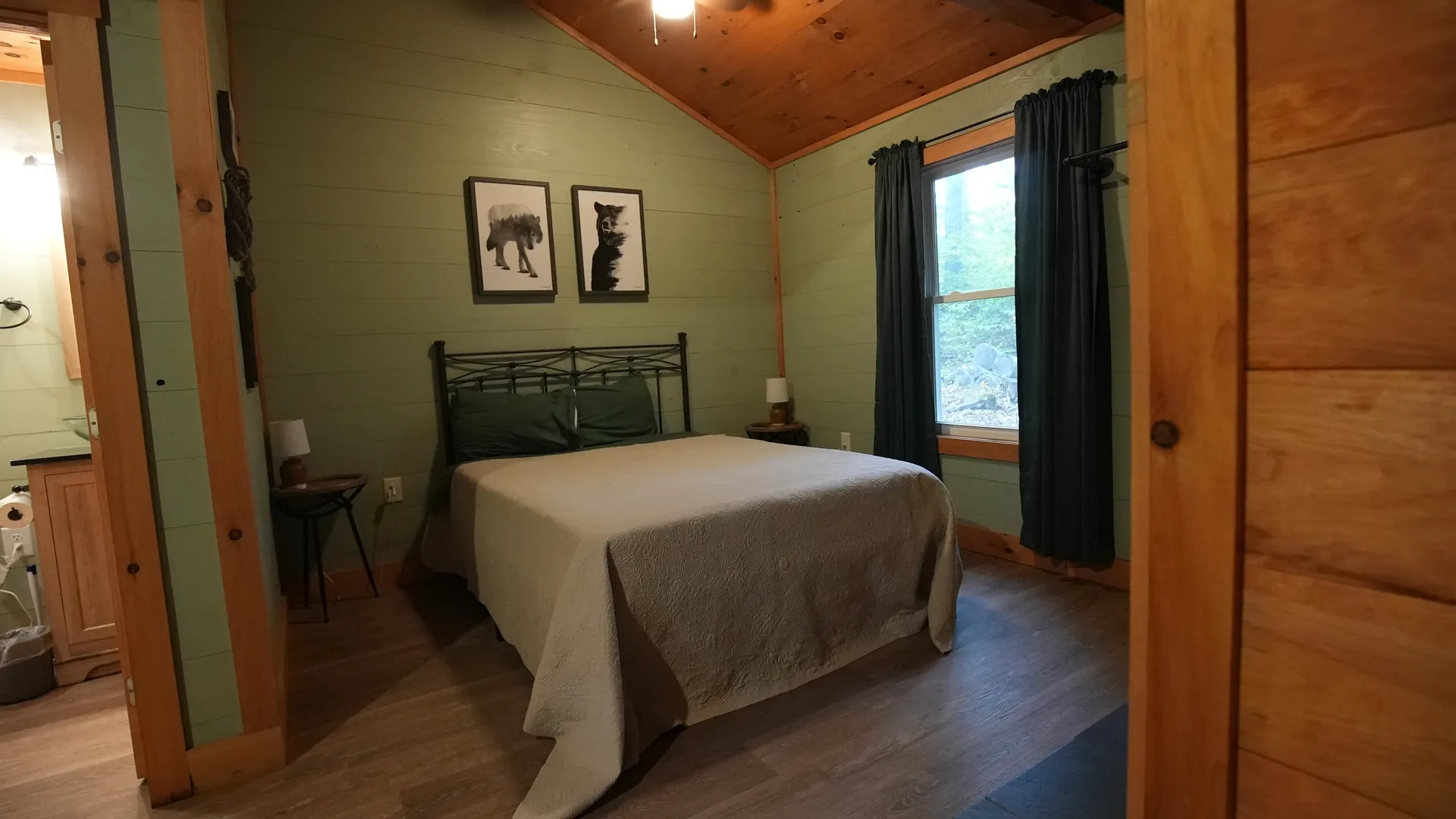 Queen bed with iron frame, white linens, bear and fox prints, and green accent wall at Forest Aisle cabin