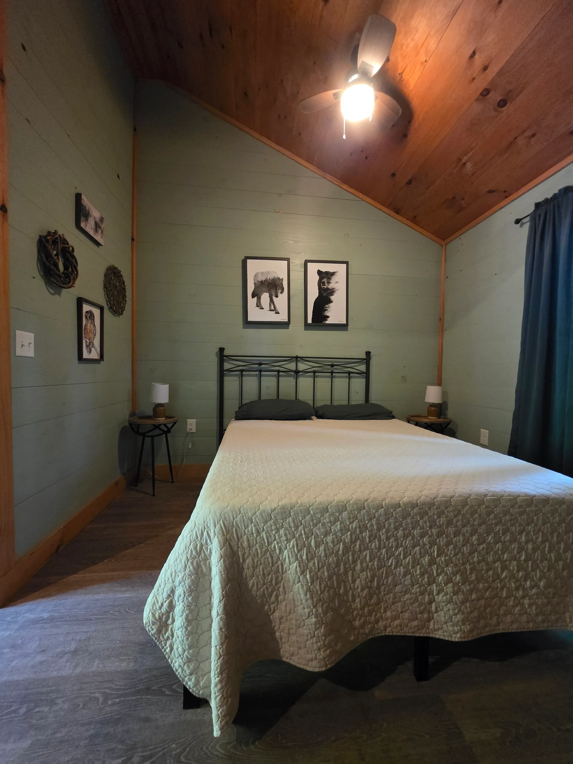 Wide bedroom view with queen bed, bear prints, side table, and wreath decor at Forest Aisle cabin