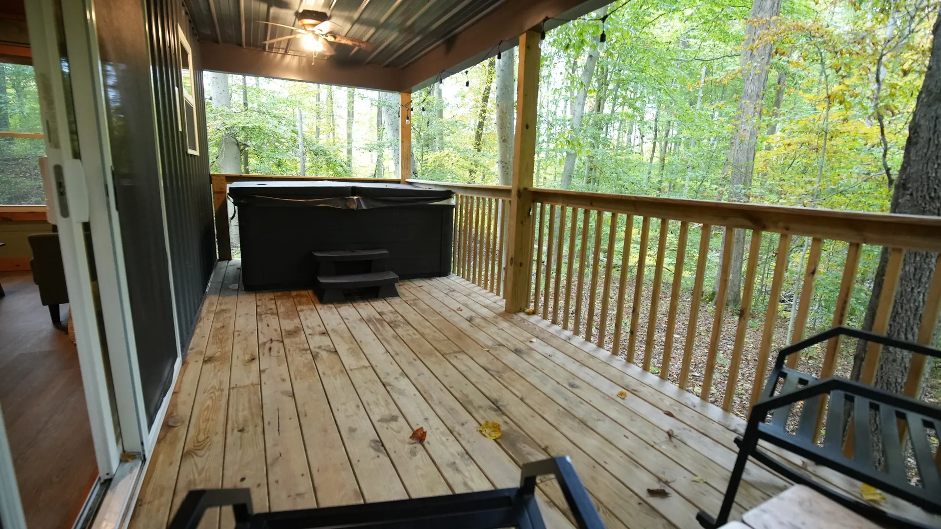 Covered deck with hot tub, rocking chairs, and string lights overlooking the autumn forest at Forest Aisle cabin