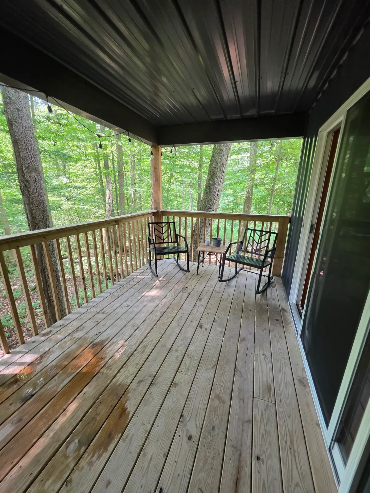 Covered deck seating area with metal chairs and forest view at Forest Aisle cabin