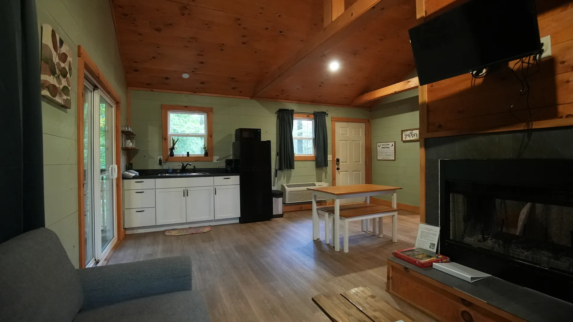 Full interior with kitchenette, dining table, fireplace, and vaulted wood ceiling at Forest Aisle cabin