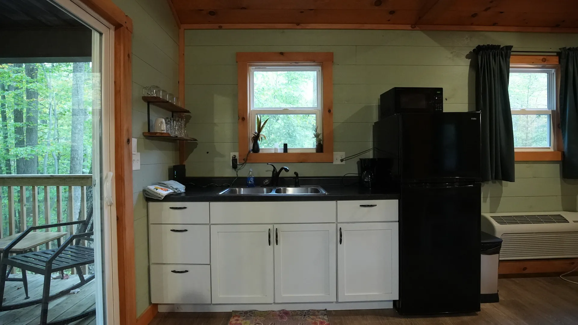 Full kitchen with white cabinets, black appliances, open shelving, and sliding door view at Forest Aisle cabin