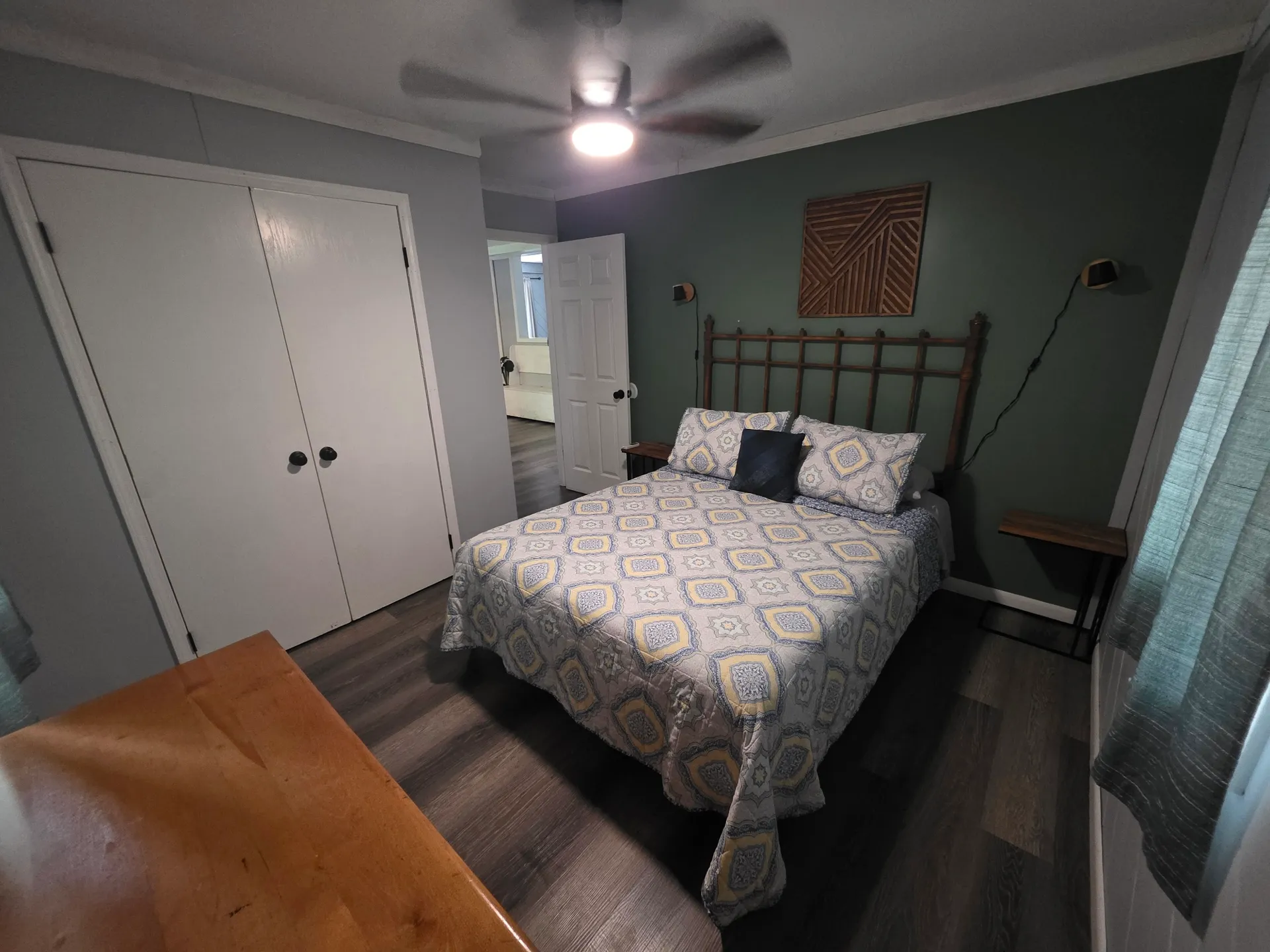 Main bedroom with queen bed, patterned bedspread, ceiling fan, and sage green accent wall at Getaway House cabin