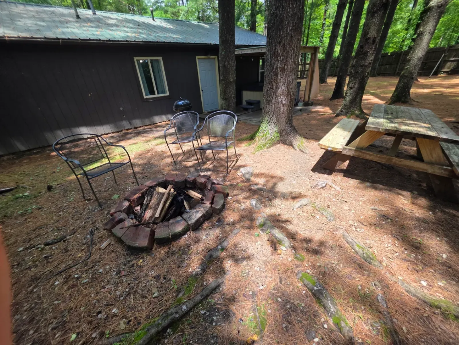 Fire pit with seating and picnic table in the wooded backyard at Getaway House cabin