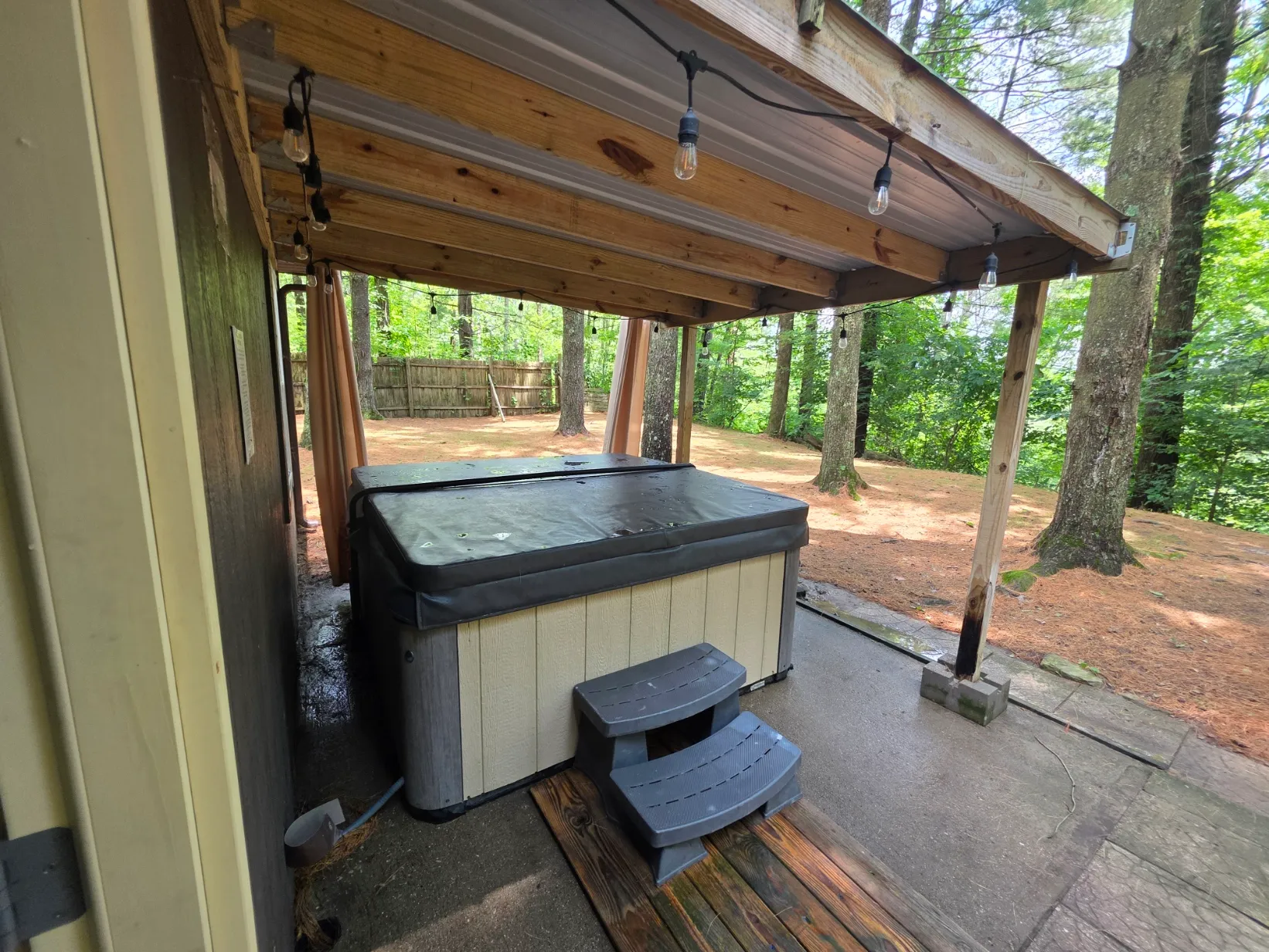 Covered hot tub with string lights surrounded by forest at Getaway House cabin