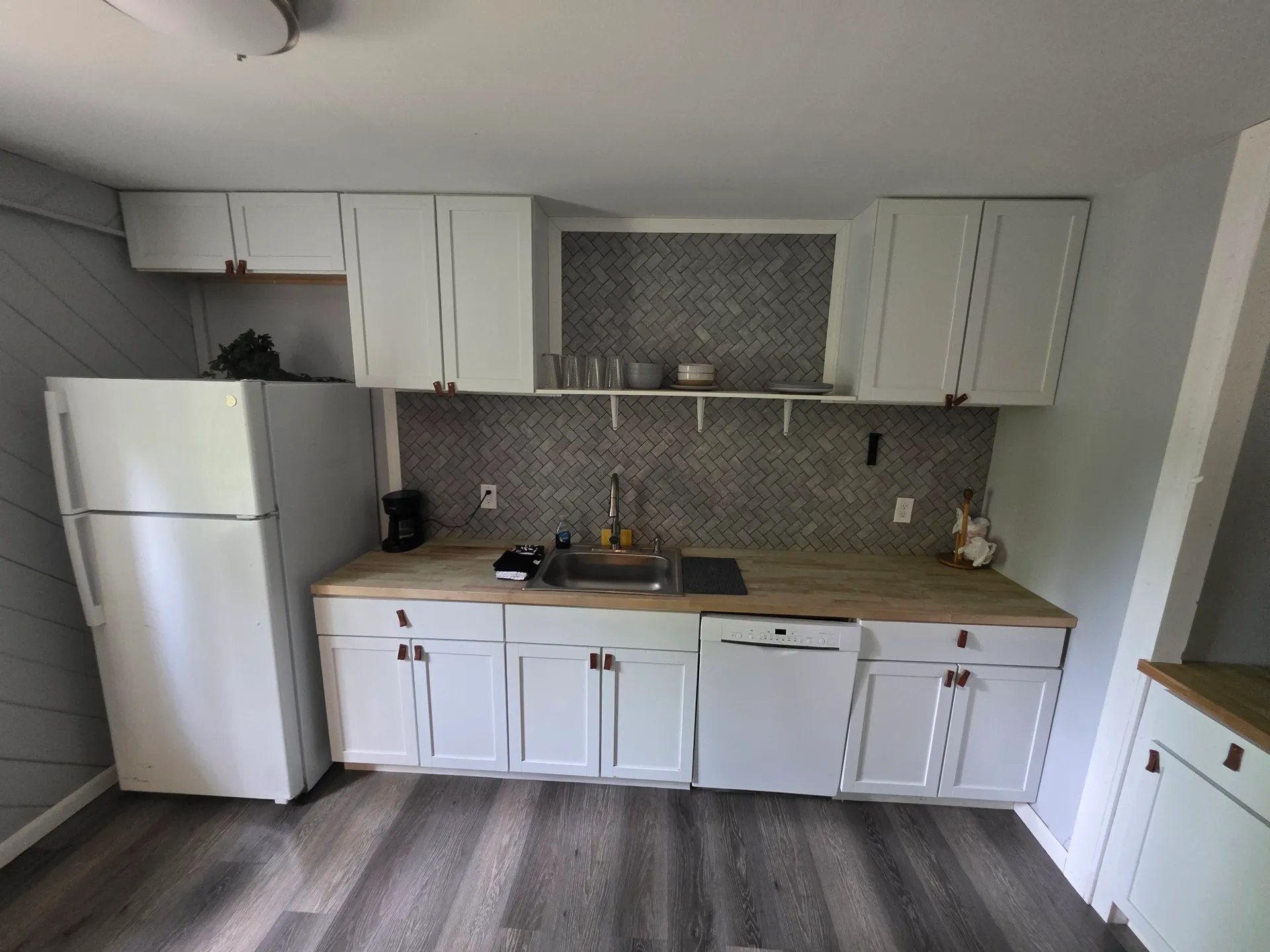 Kitchen with white cabinets, dishwasher, and herringbone tile backsplash at Getaway House cabin