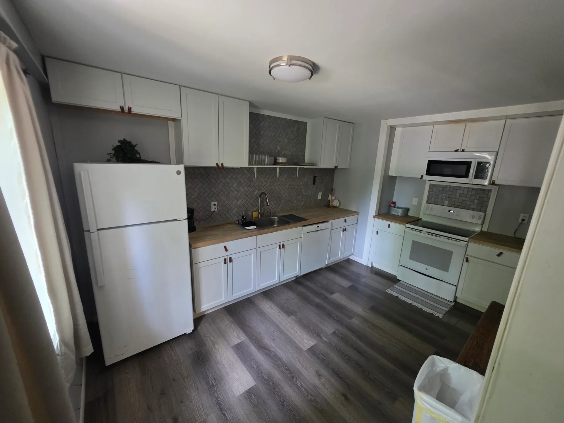 Full kitchen with white cabinets, herringbone tile backsplash, and butcher block countertops at Getaway House cabin