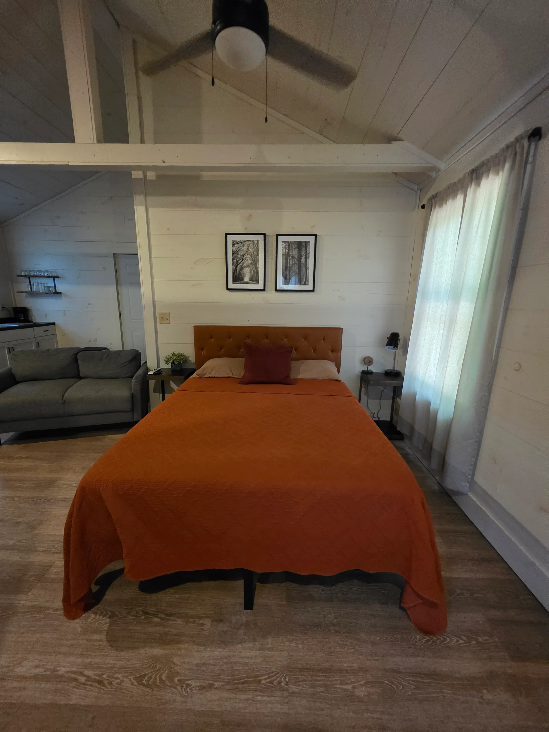 Queen bed with burnt orange quilt, tufted headboard, and framed prints at Hummingbird cabin