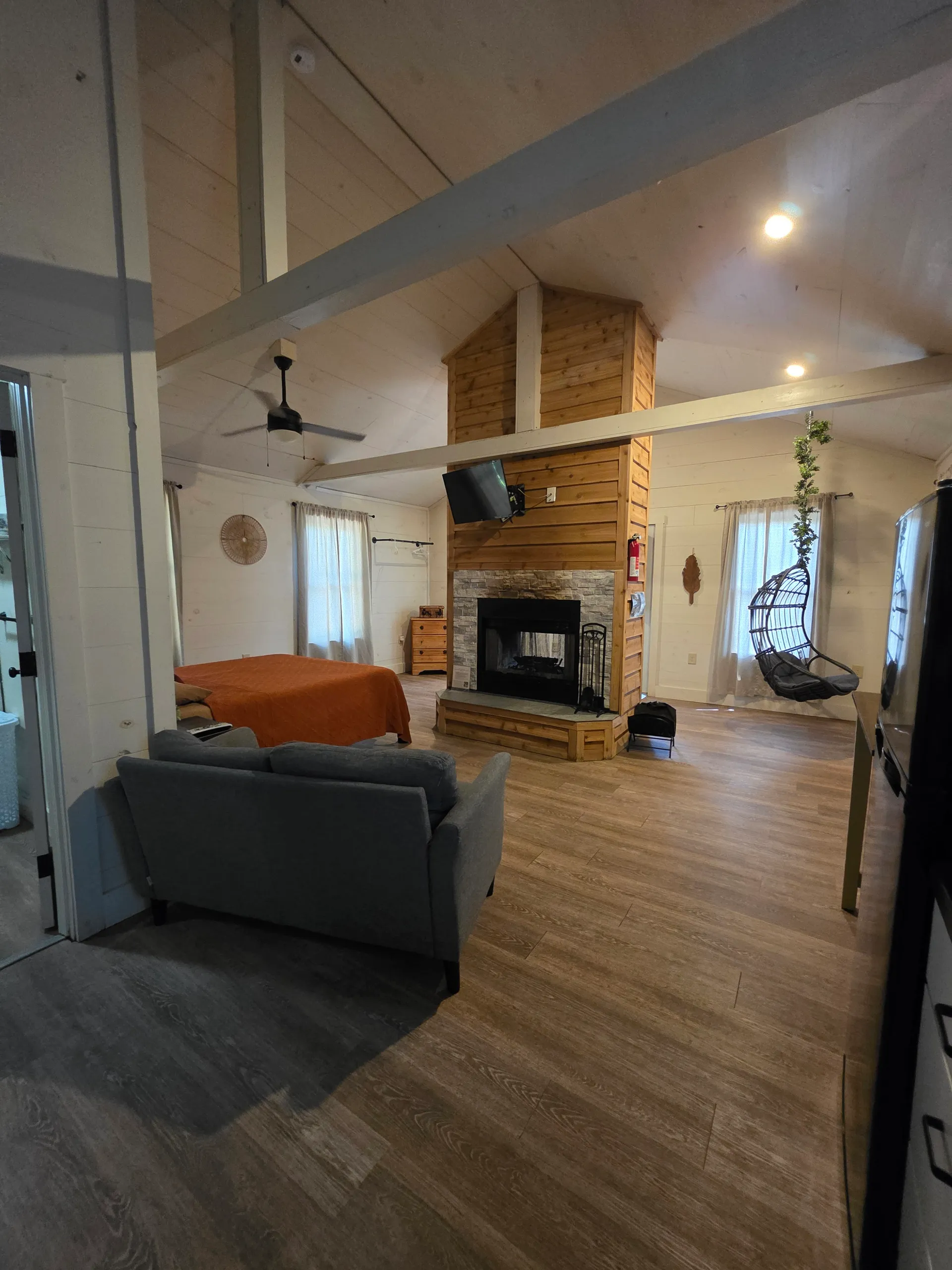 Wide-angle interior showing living room, fireplace, hanging chair, and vaulted ceiling at Hummingbird cabin