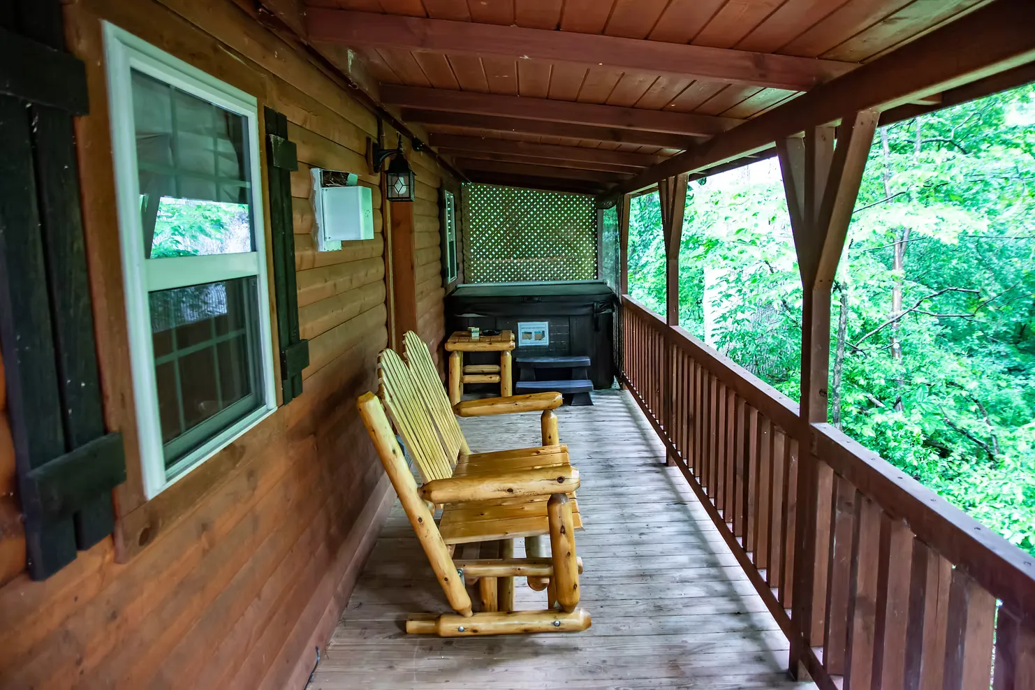 Covered front porch with log rocking chairs and hot tub at Millers Den cabin