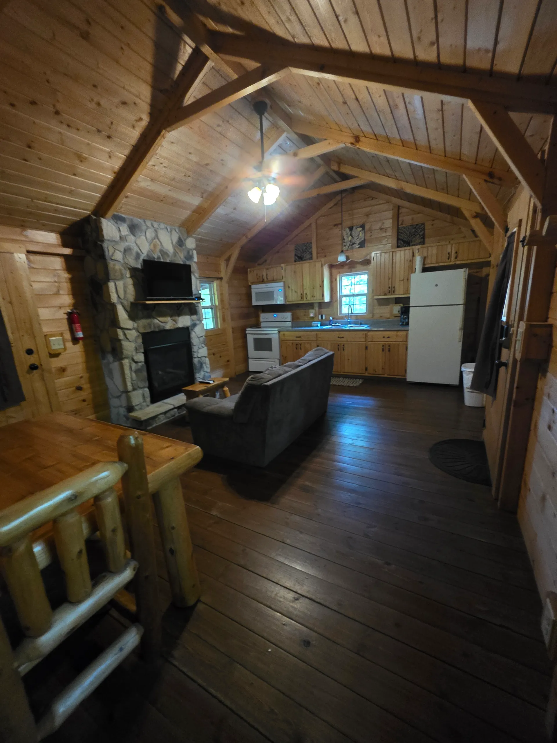Open-plan living room with stone fireplace and kitchen viewed from loft at Millers Den cabin