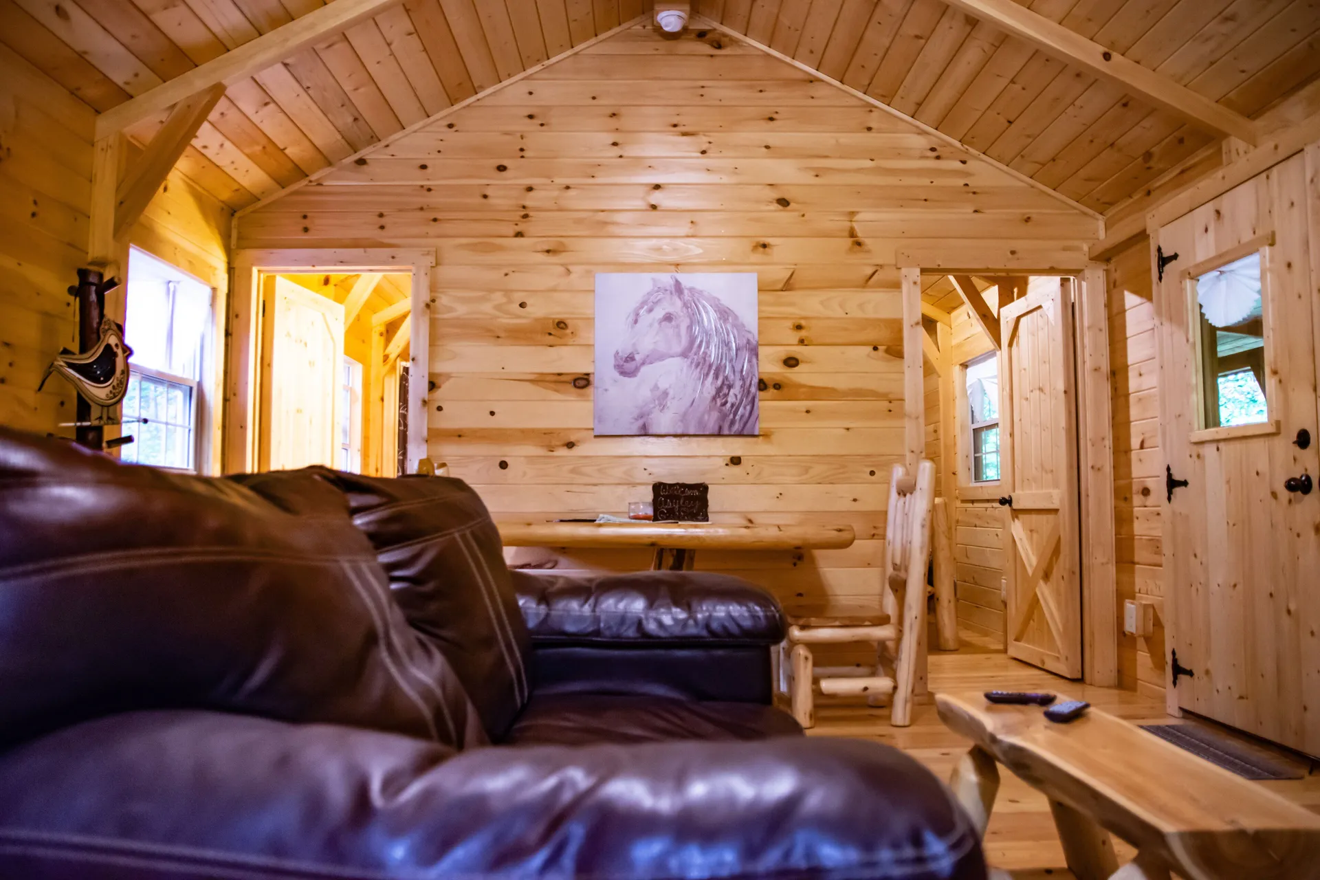 Upper living area with leather sofa, horse artwork, and pine walls at Millers Den cabin
