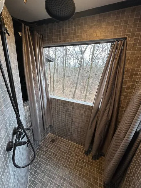Tiled walk-in shower with rainfall showerhead and large forest view window at Moonshiner cabin