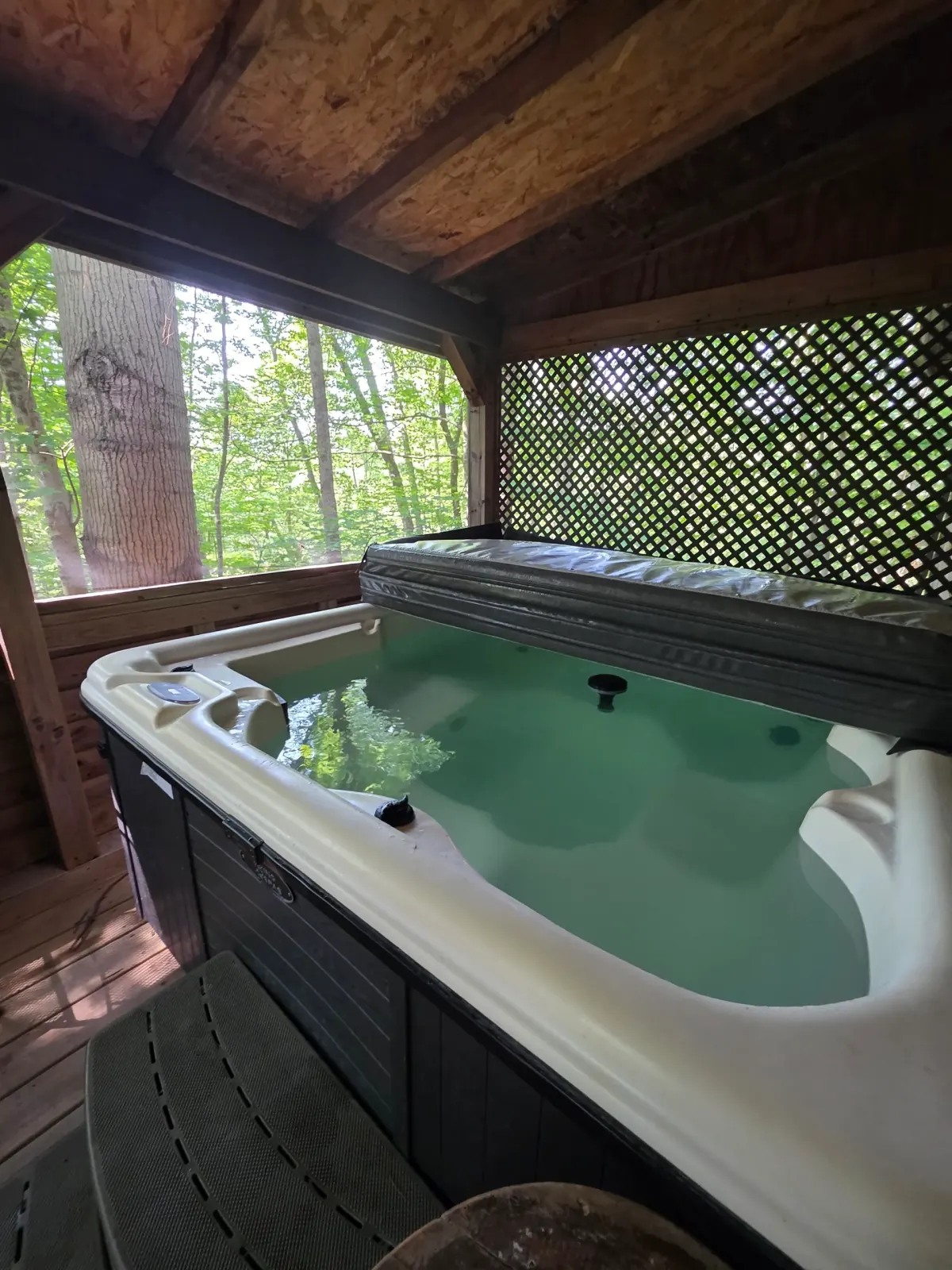 Close-up of hot tub with forest views through lattice screening on covered deck at Moonshiner cabin