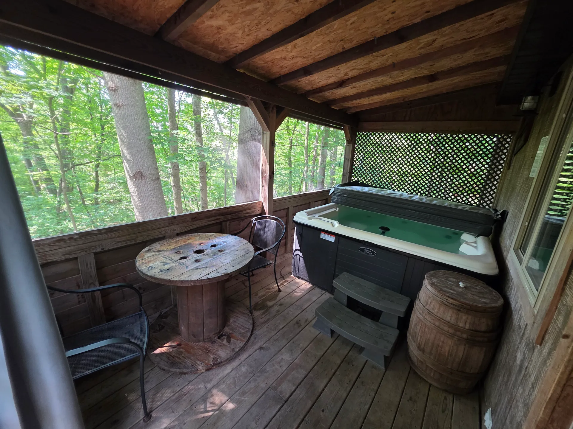 Hot tub with spool table and whiskey barrel on covered forest deck at Moonshiner cabin