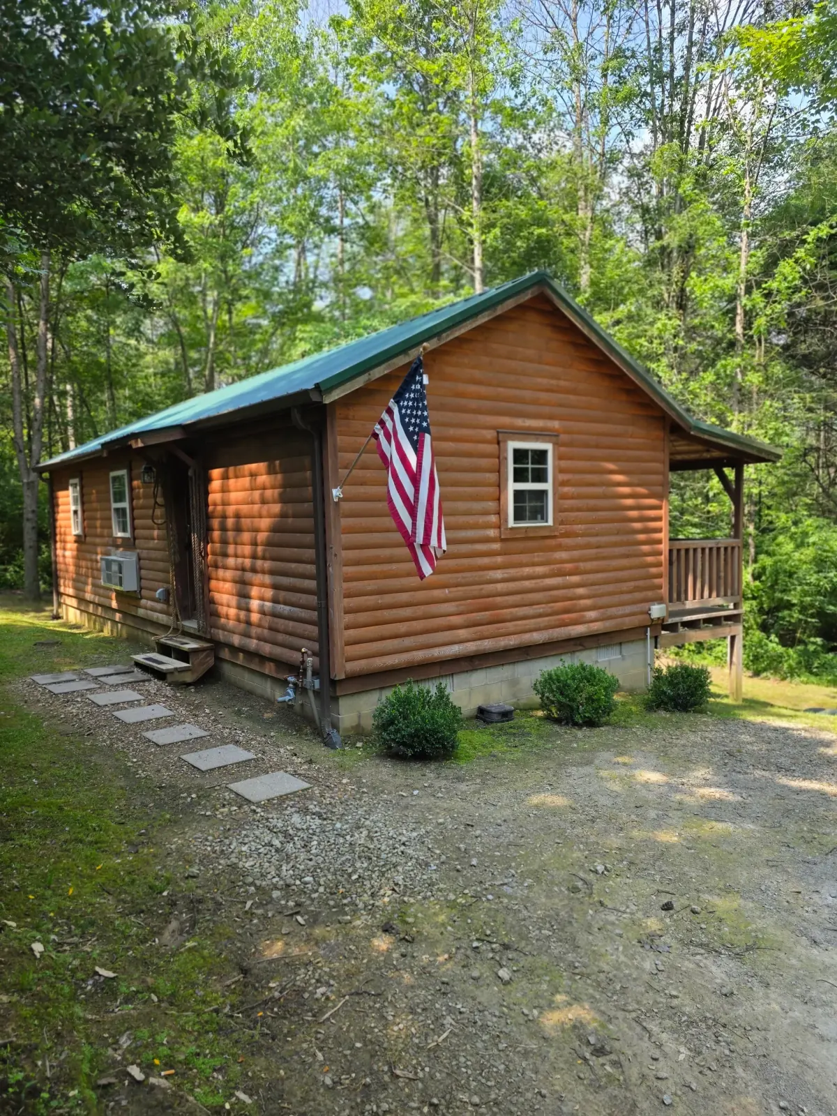 Front view of Settlers Roost log cabin with American flag and covered porch surrounded by lush green forest