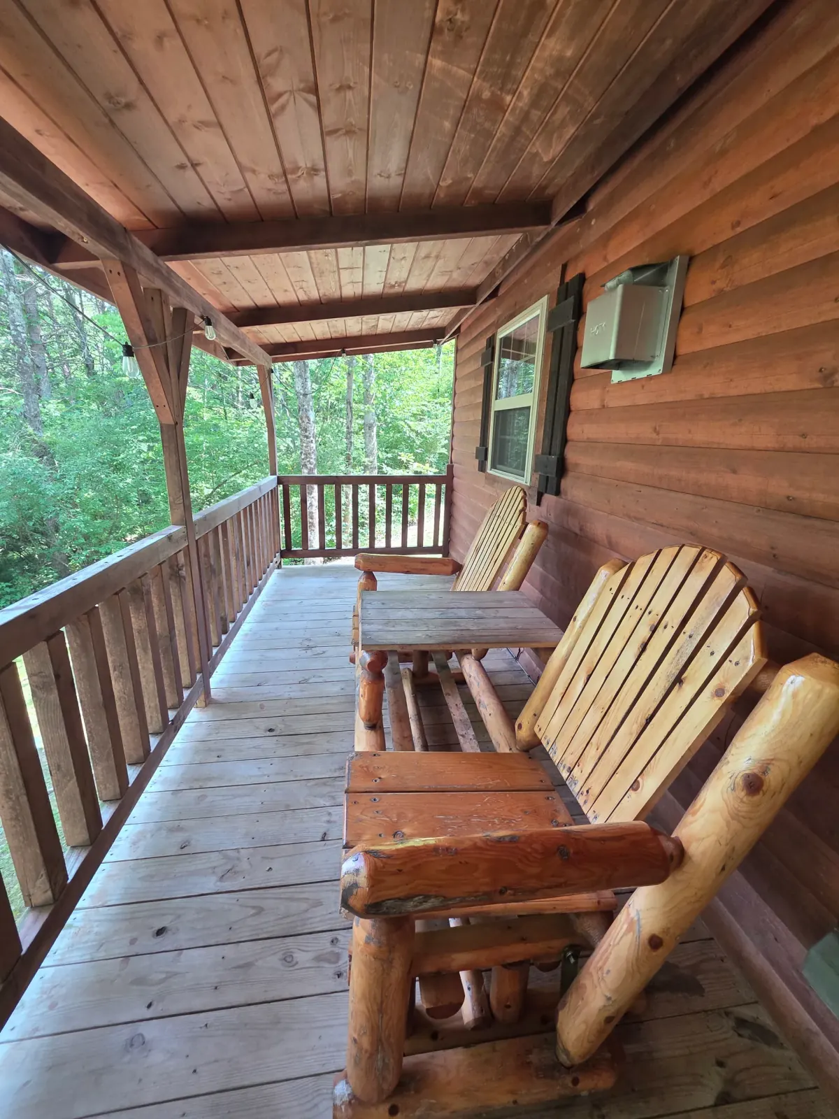 Covered back deck with log railing and ceiling fan overlooking the woods at Settlers Roost cabin