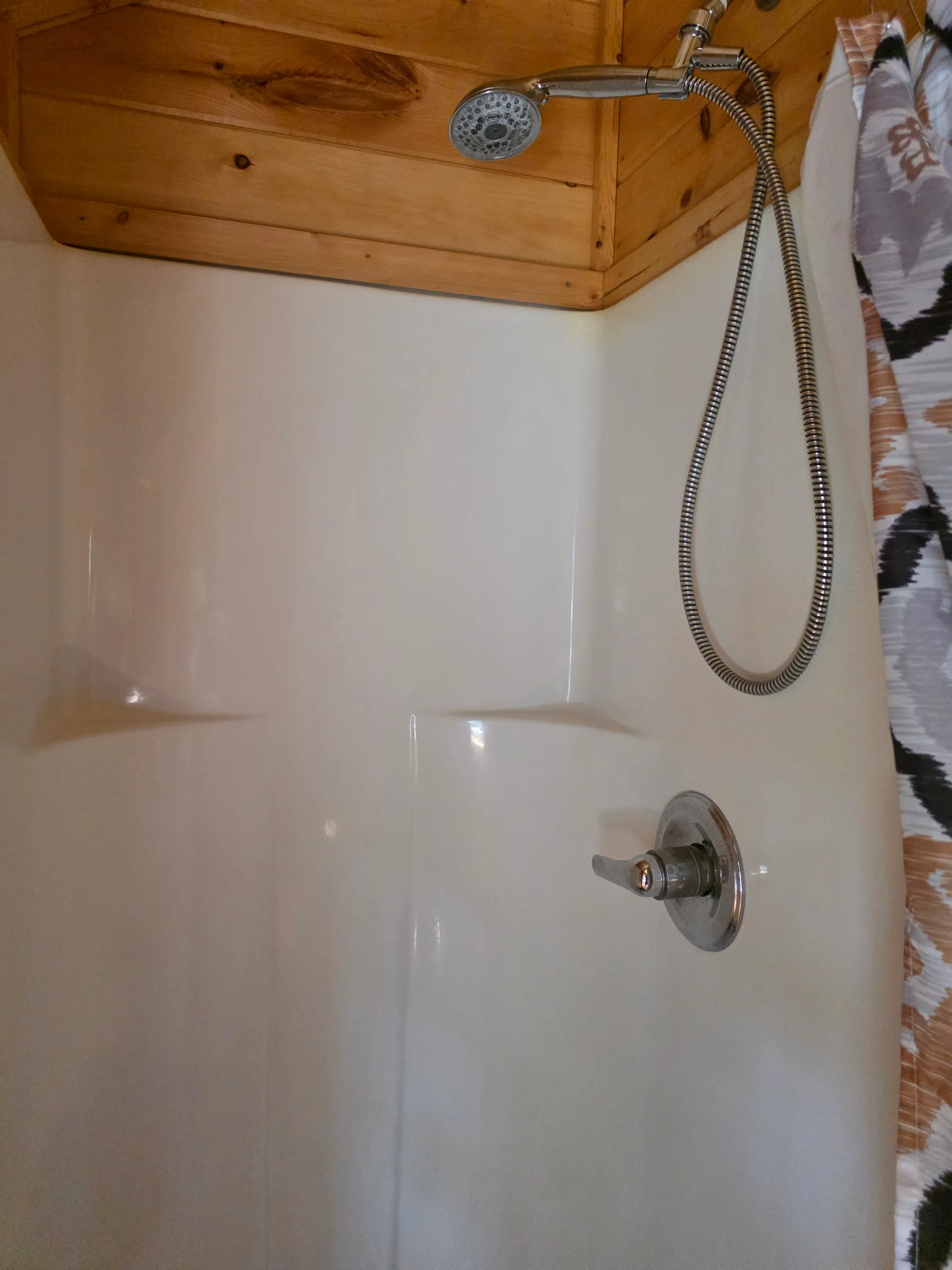 Bathtub with handheld shower head in the wood-paneled bathroom of Settlers Roost cabin