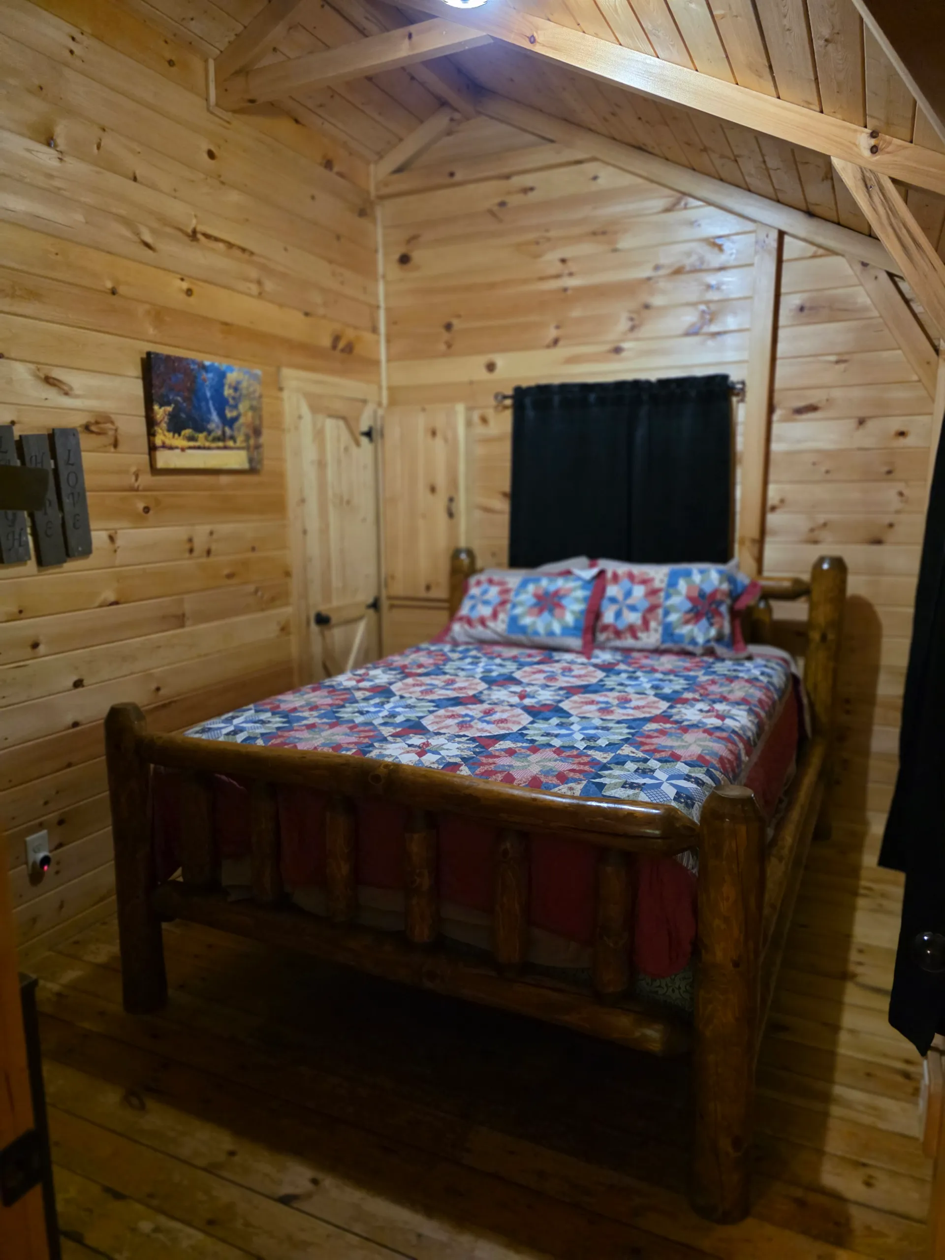 Cozy bedroom in Settlers Roost cabin with queen log bed, patchwork quilt, and warm pine walls