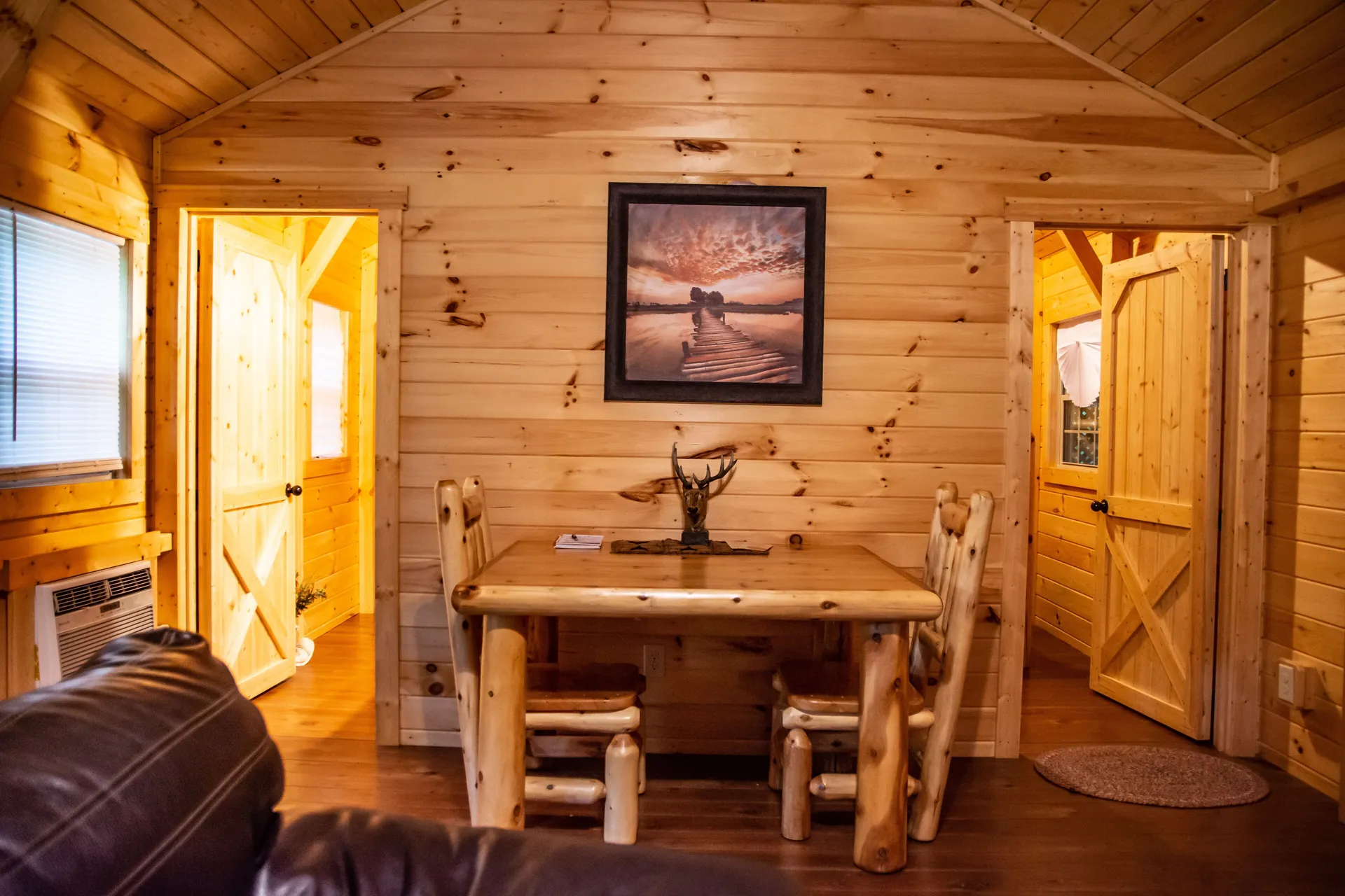 Rustic log dining table and chairs with western artwork on pine-paneled walls inside Settlers Roost cabin