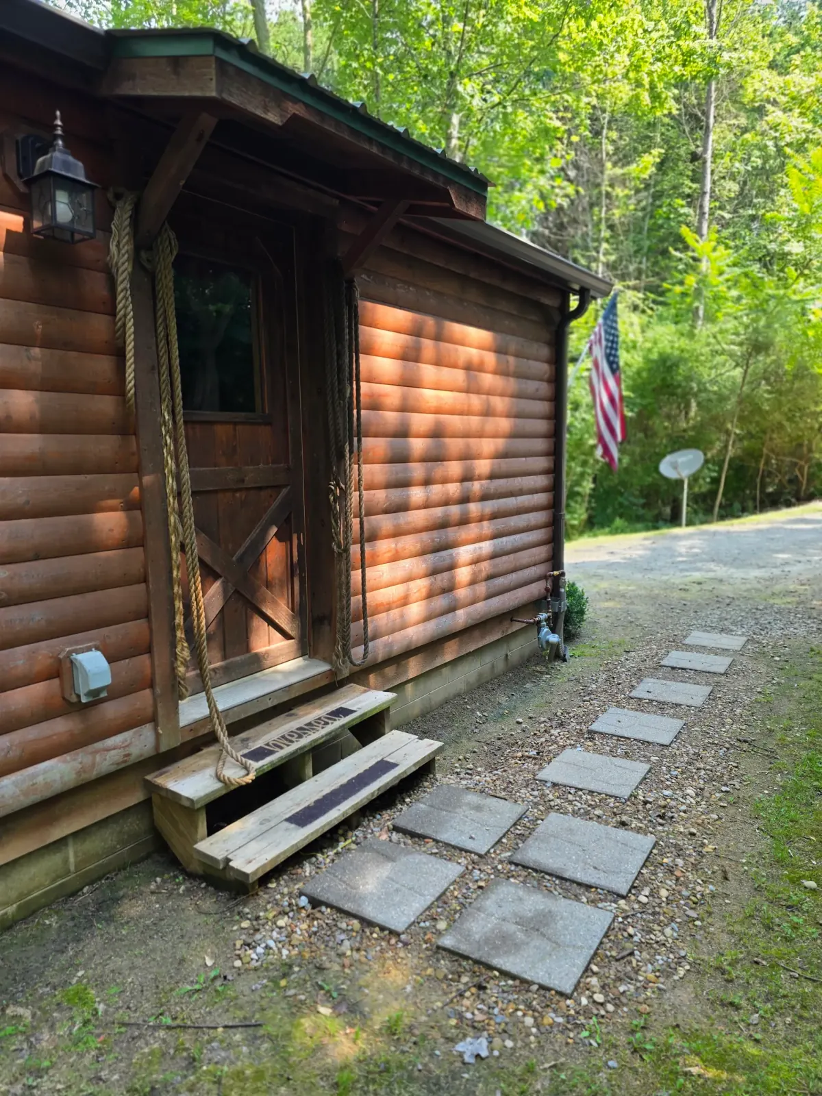 Settlers Roost cabin front entry with covered porch, rope hammock, stone walkway, and American flag