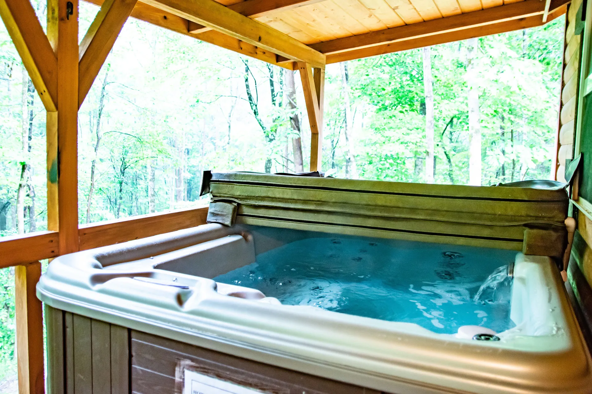 Bubbling hot tub on the covered wooden deck at Settlers Roost cabin with panoramic views of the Hocking Hills forest