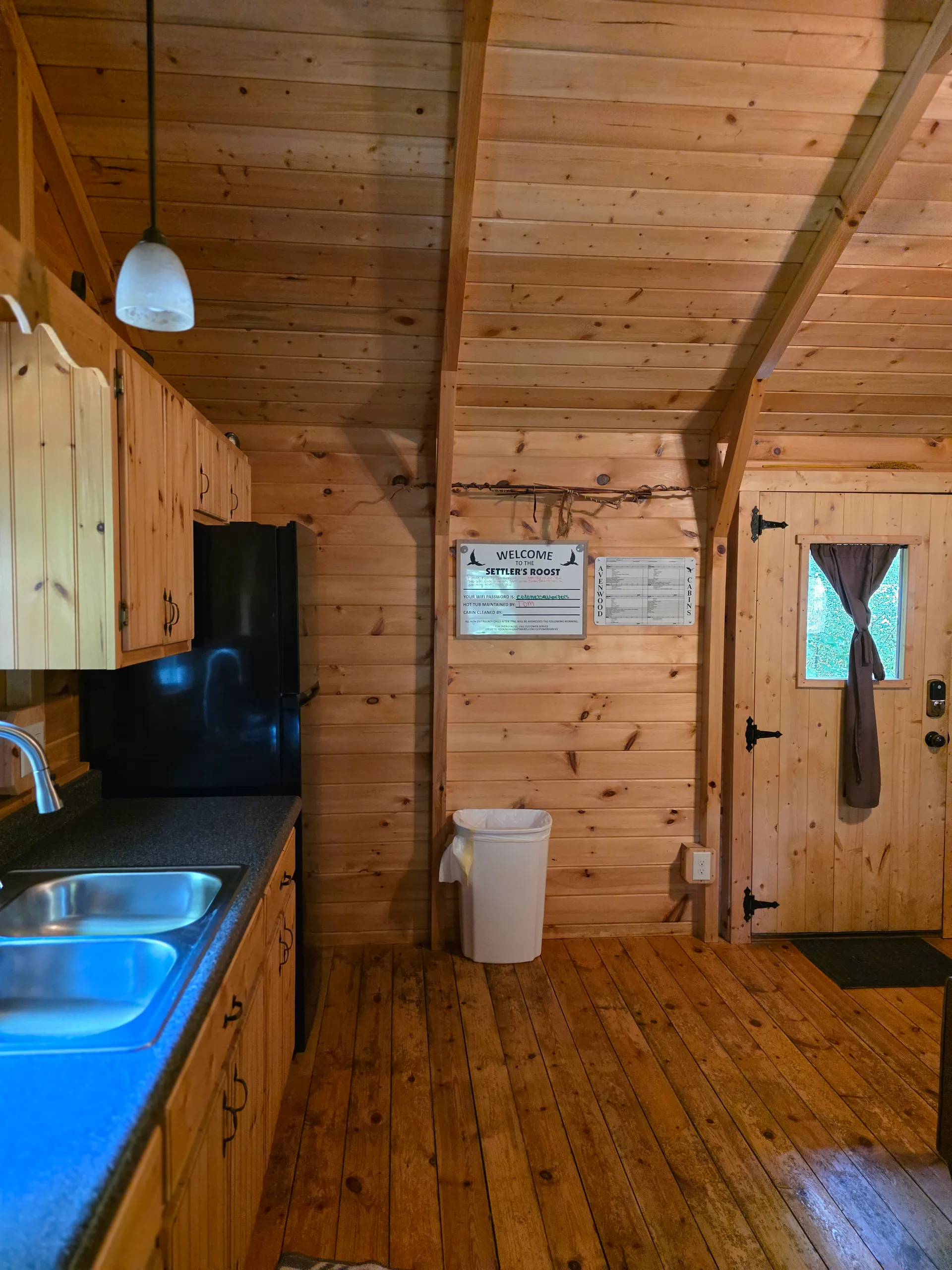 Kitchen and living area overview inside Settlers Roost cabin showing pine cabinets, countertops, and welcome sign