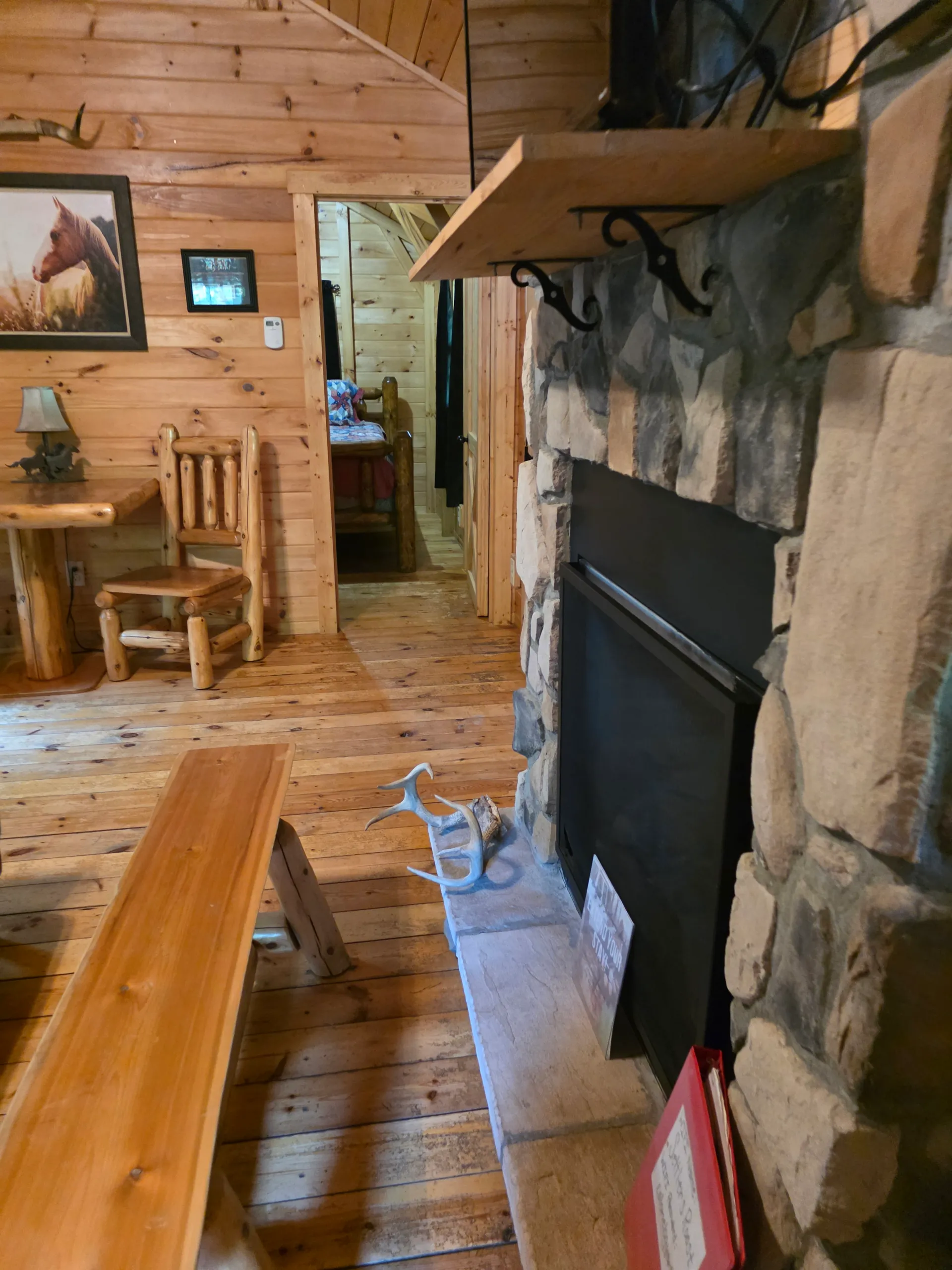 Stone fireplace with antler decor, log dining set, and western art viewed from the living room of Settlers Roost cabin